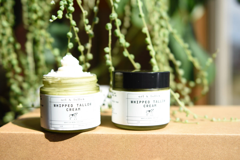 Two jars of whipped talcum cream on a wooden surface with greenery in the background